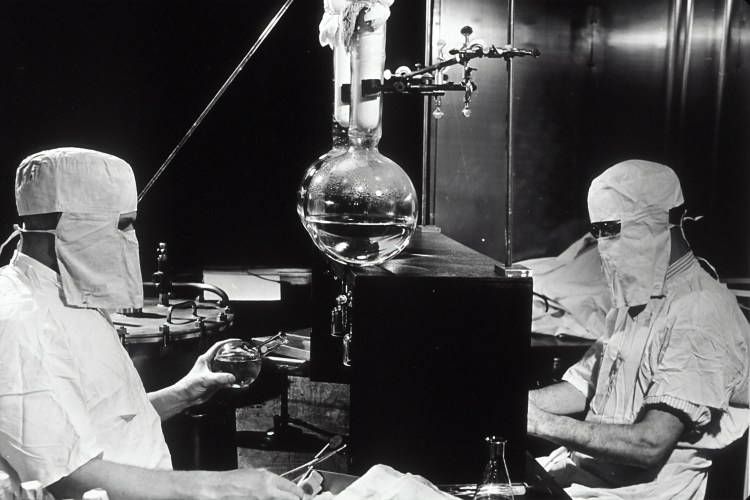 Generic laboratory shot circa 1950 - researchers garbed with full mask and head covering and laboratory equipment.